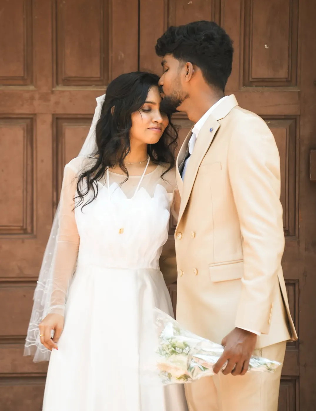 Bride in a white gown and veil with groom against wooden doors