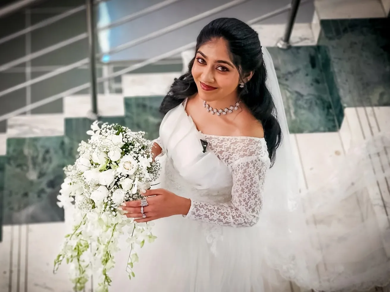 Bride on marble stairs holding a white bouquet
