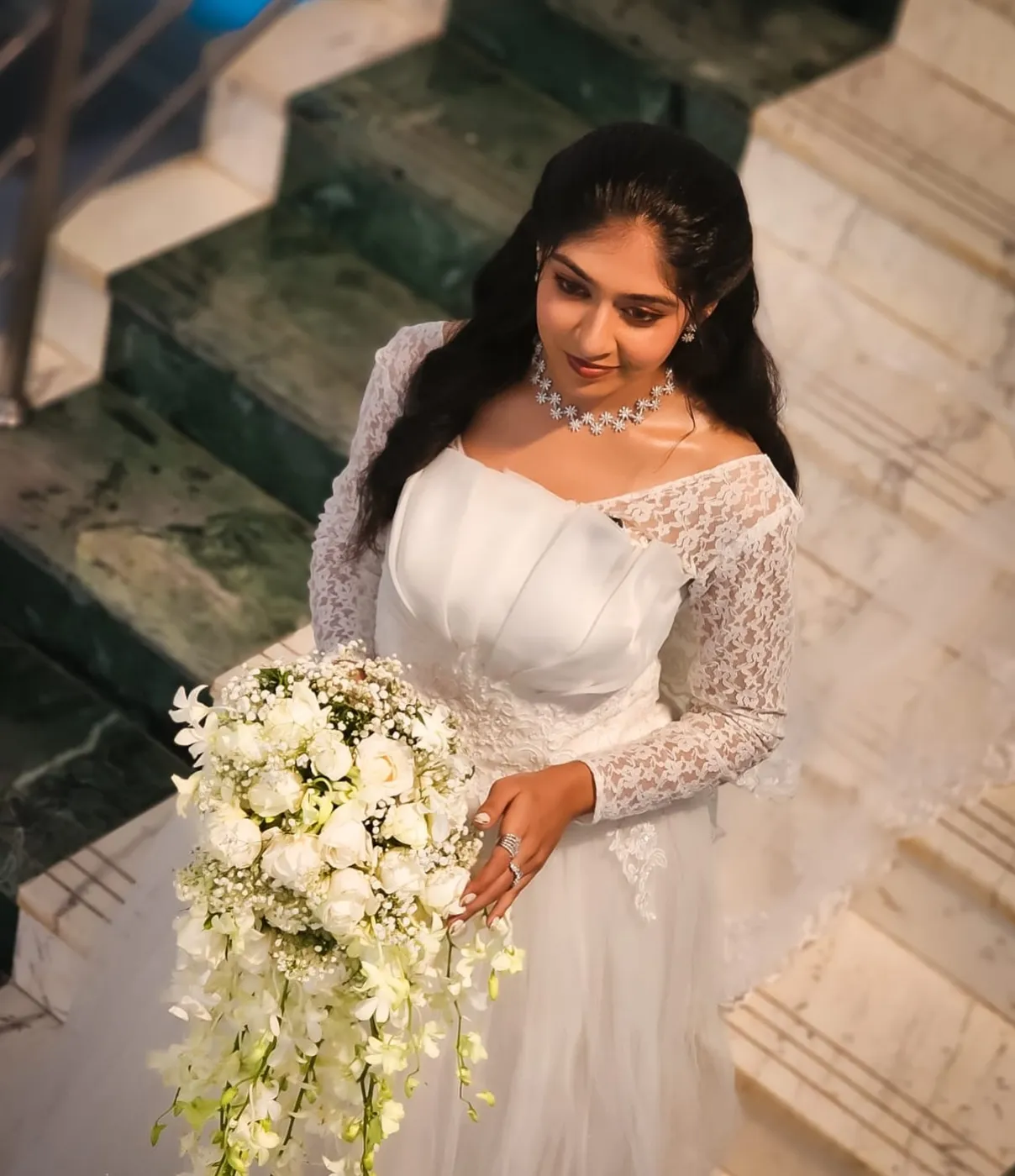 Bride in a lace-sleeved white gown holding a cascade bouquet